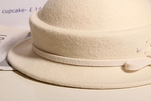 Detail of wool felt cloche hat with ribbon bow, pearl accents and floral decoration