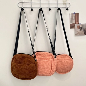 Lambswool crossbody bags in brown and pink colors with adjustable straps hanging on a wall