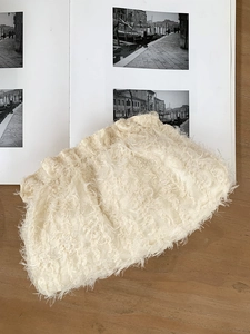 Détail de la pochette nuage à franges blanc cassé posée sur un livre et table en bois