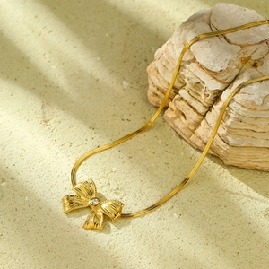 Collana a fiocco dorata con zircone e catena a serpente su sfondo di sabbia naturale