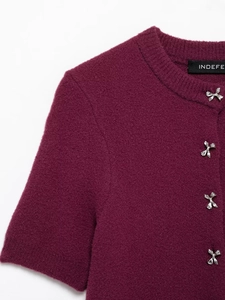 Detail of burgundy knit cardigan featuring silver bow buttons and ribbed crew neck