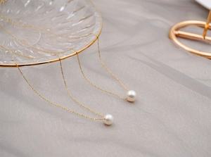 Detail of single pearl pendant necklaces on gold chain draped over a glass tray