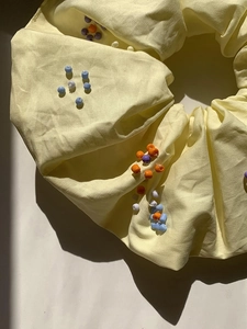 Dettaglio macro dello scrunchie in tessuto giallo con decorazioni di perle fatte a mano