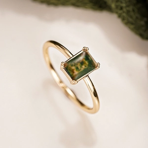 Macro view of a gold-plated ring featuring rectangular green stone in a classic 4-prong setting