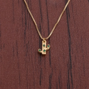 Close-up of gold cactus pendant necklace with green zircons on a rustic wood background