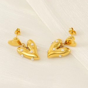 Close-up of golden heart-shaped earrings with white pearls on elegant silk fabric