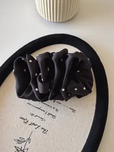 Close-up of elegant black and white polka dot satin scrunchie with pleated texture