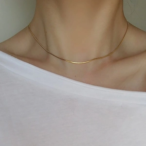Close-up of a minimalist gold snake bone chain necklace worn by a female model