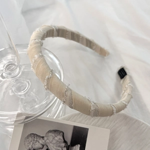 Artistic detail of cream sponge headband with frayed edge fabric on soft white fabric