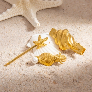 Three-piece gold stainless steel hair clips set with seashells and starfish on beach sand