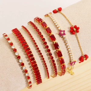 Detail view of seven gold tennis bracelets with red and white zircons on a beige display