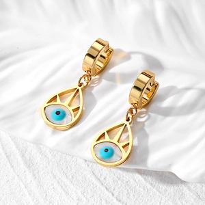 Detail view of golden evil eye drop earrings on a white aesthetic textured display tray