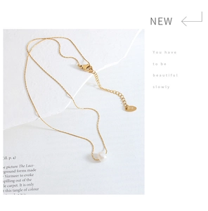 Detail shot of K18 engraved metal tag and fine gold chain with freshwater pearl