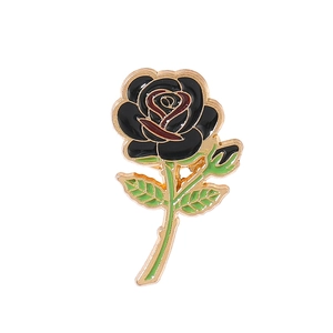 Close-up of black rose brooch with red details and green leaves in golden metal trim