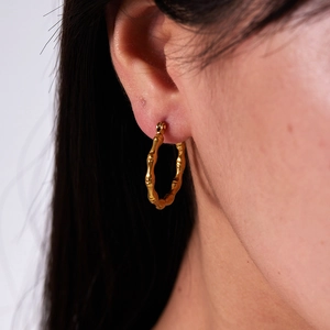 Gros plan de boucles d'oreilles créoles en bambou doré 18 carats portées par un mannequin