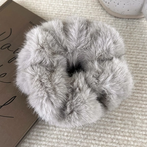 Close-up of soft grey plush scrunchie with fluffy faux mink texture on beige rug
