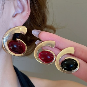 Detail of elegant C-shaped gold metal earrings featuring large oval red and black gemstones