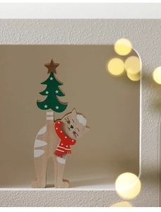 Detail of wooden Christmas cat ornament with red scarf and green tree on a table