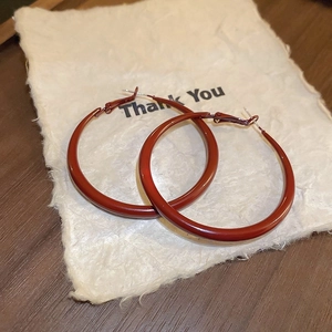 Close-up of vibrant red metallic hoop earrings on a decorative Thank You card