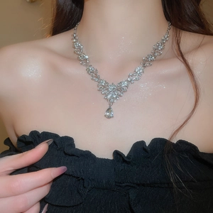 Detailed close-up of a silver rhinestone leaf necklace with a teardrop pendant on model