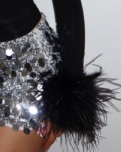 Détail d'une mini-jupe à paillettes argentées et manches noires à plumes denses