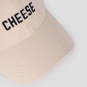Makro-Detail der hochwertigen schwarzen 'CHEESE' Stickerei auf beige Baumwollkappe