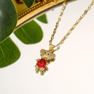 Artistic close-up of golden teddy bear necklace with red heart stone and micro-pave zircons
