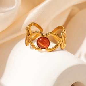 Détail d'une bague coeur dorée avec oeil de chat rouge sur fond de soie champagne