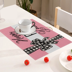 Detail shot of a pink rectangular placemat featuring a black and white bow and Happy text