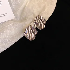 Minimalist silver wavy rhombus stud earrings with metallic ripple texture on paper