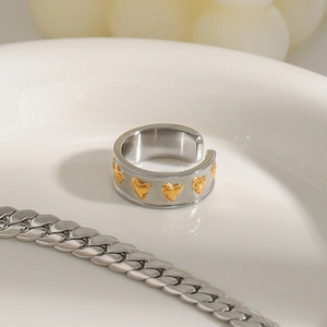 Détail d'une bague large ouverte en acier argenté avec motifs de cœurs dorés