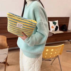 Close-up of fluffy yellow and blue striped plush makeup bag with woven brand label