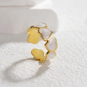 Makroaufnahme: Goldener geometrischer Ring mit weißem Emaille-Herz-Inlay und Glanz