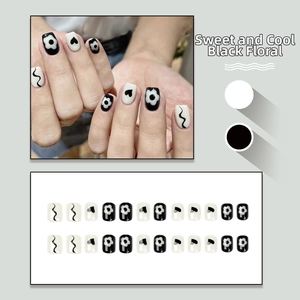 Detail of black and white press-on nails with floral and heart patterns in square-oval shape