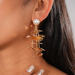 Detail of long gold ginkgo leaf earrings with pearl stud on model's profile