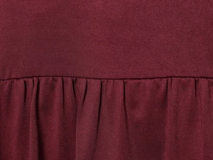 Detaillierte Nahaufnahme von dunkelrotem Strickstoff mit eleganter Faltenstruktur und Naht
