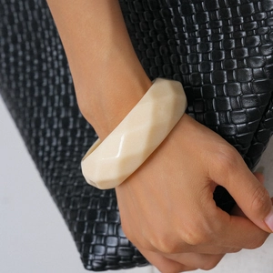 Macro shot of cream resin faceted geometric bangle worn on wrist against leather bag