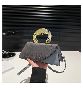 Detail of grey spliced leather handbag with unique gold metal handle and slim strap