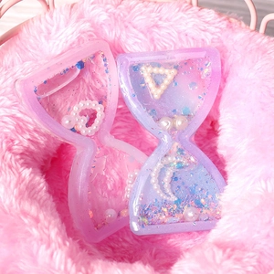 Macro shot of hourglass-shaped resin keychains with pink and purple glitter on pink fur