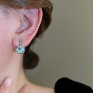 Close-up of square cut sea blue gemstone earrings with sparkling zircon accents on model