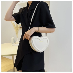 Vue détaillée du sac bandoulière blanc en forme de cœur avec texte doré sur blazer noir