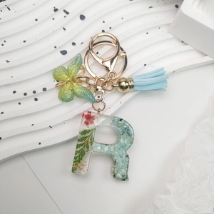 Macro shot of resin letter R keychain with dried flowers, green butterfly, and blue tassel