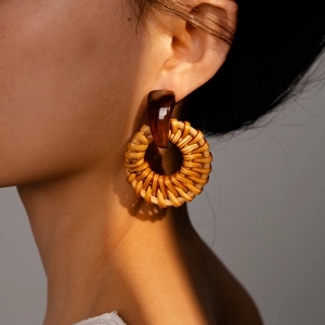 Detail view of woven resin earrings on a model with warm lighting and soft shadows