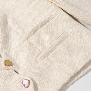 Dettaglio della giacca in tweed crema con trama in rilievo e bottoni colorati a forma di cuore