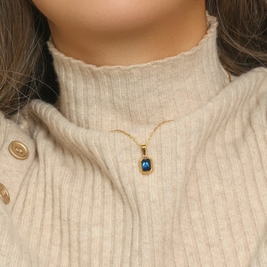 Close-up of golden paperclip chain necklace with a dark blue square zircon pendant