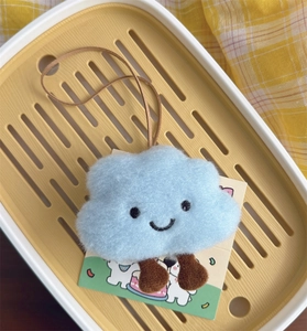 Macro shot of cute light blue plush cloud charm with embroidered smile and hanging strap