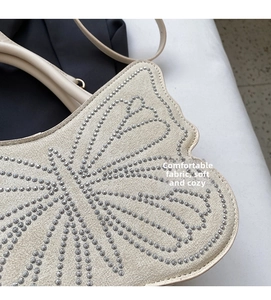 Detail of studded butterfly pattern on beige suede tote bag with soft fabric texture