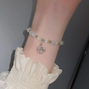 Detail eines Perlenarmbands mit weißen Opalsteinen und goldenem Kristallanhänger
