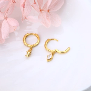 Detail of gold huggie hoop earrings with marquise white zircon on a white plate