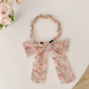 Close-up of pink floral headband woven with gold chains and pearls with a large bow